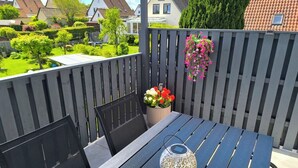 A balcony with a table, chairs, a decorative vase with flowers, and a view of houses and greenery. - Beautiful large apartment with super roof terrace (Walsrode)
