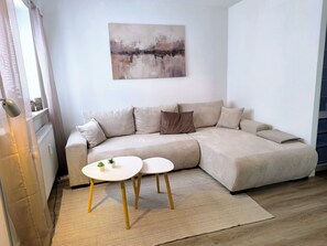Ein modernes Wohnzimmer mit einem beigefarbenen Sofa, einem kleinen weißen Tisch und einem großen abstrakten Gemälde an der Wand.