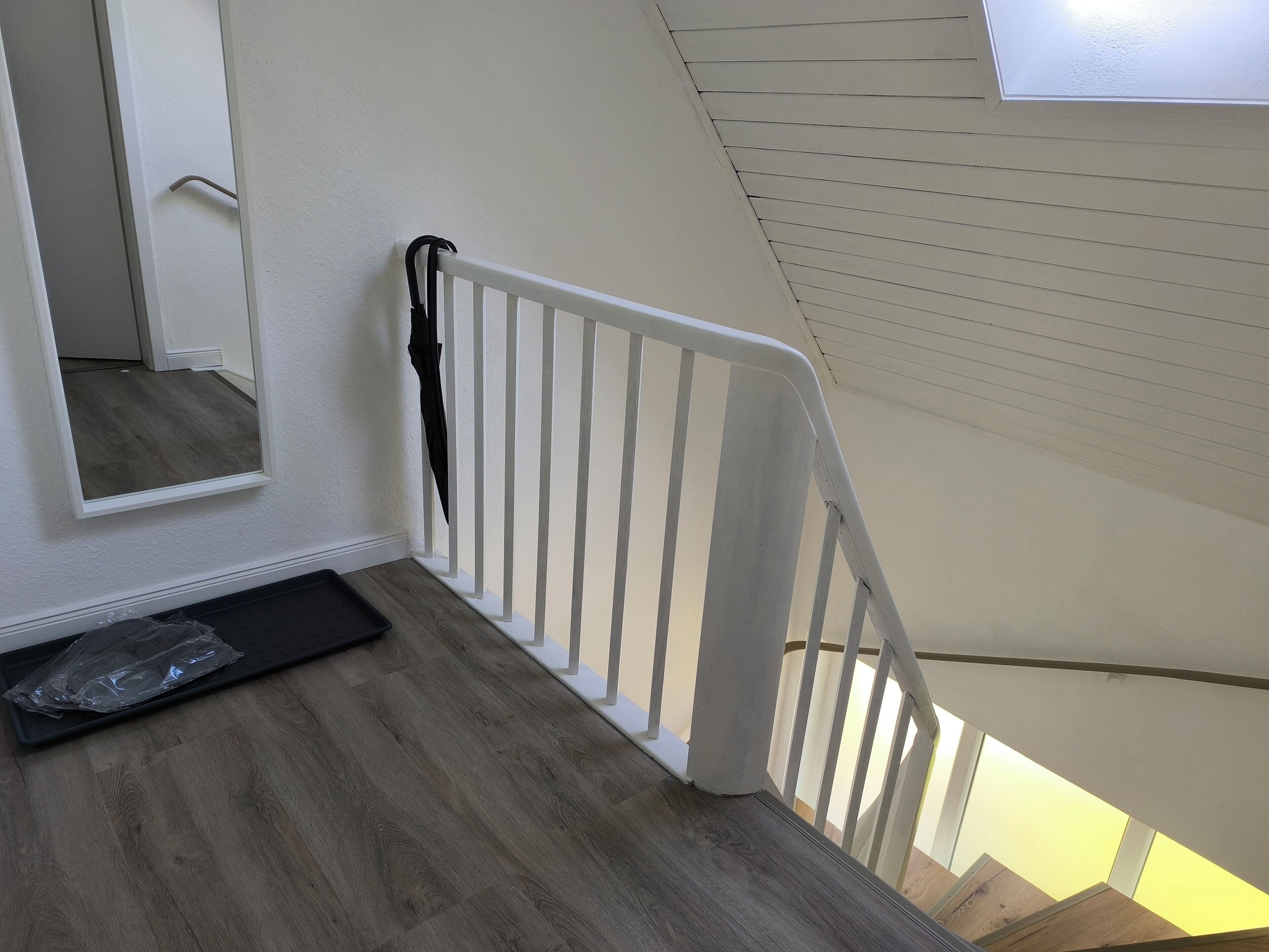 A staircase with a white railing, a wooden floor, and a black mat at the base.