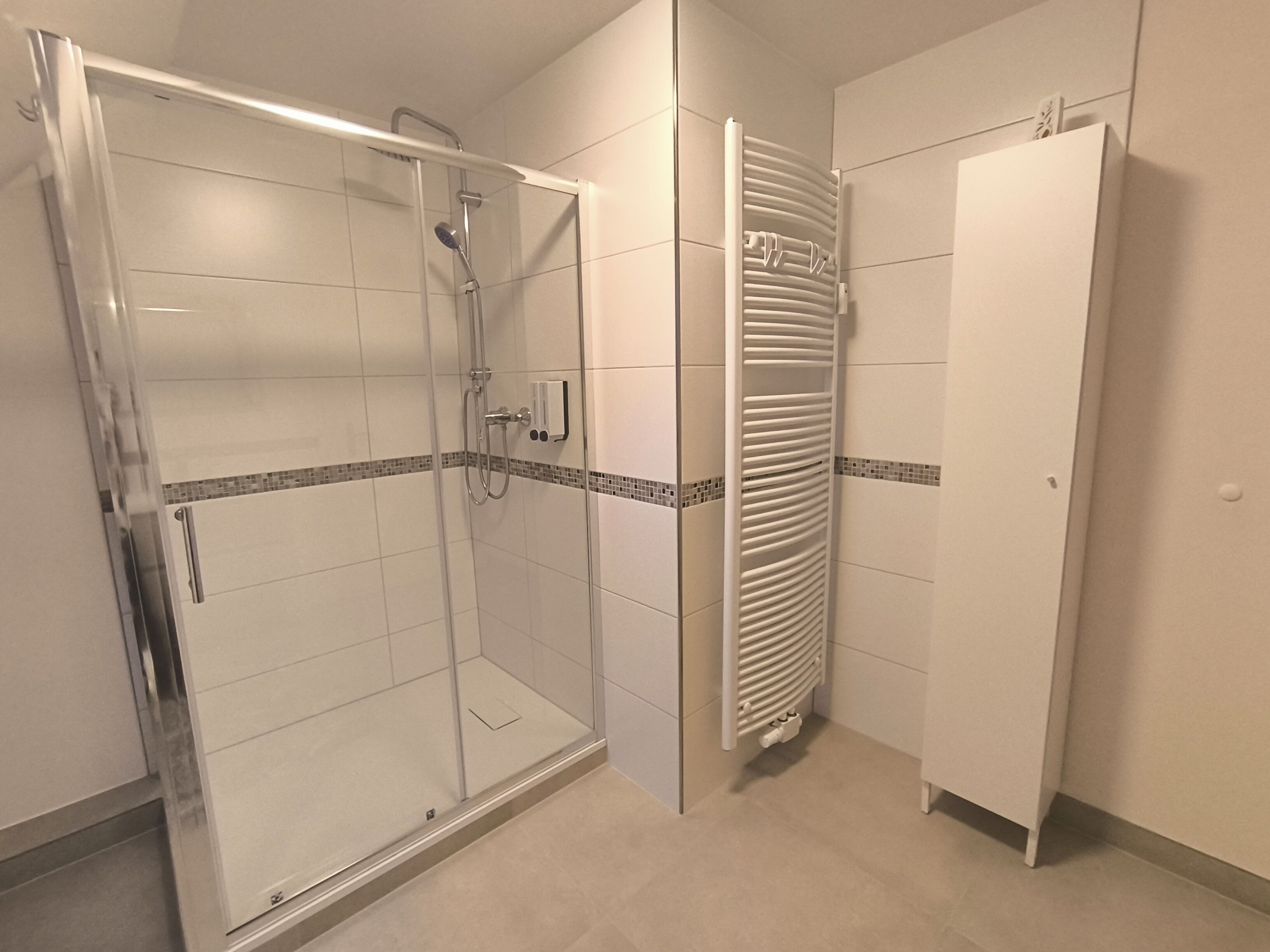 Eine Duschkabine mit Handbrause, einem Handtuchhalter und einem weißen Schrank mit Tür.