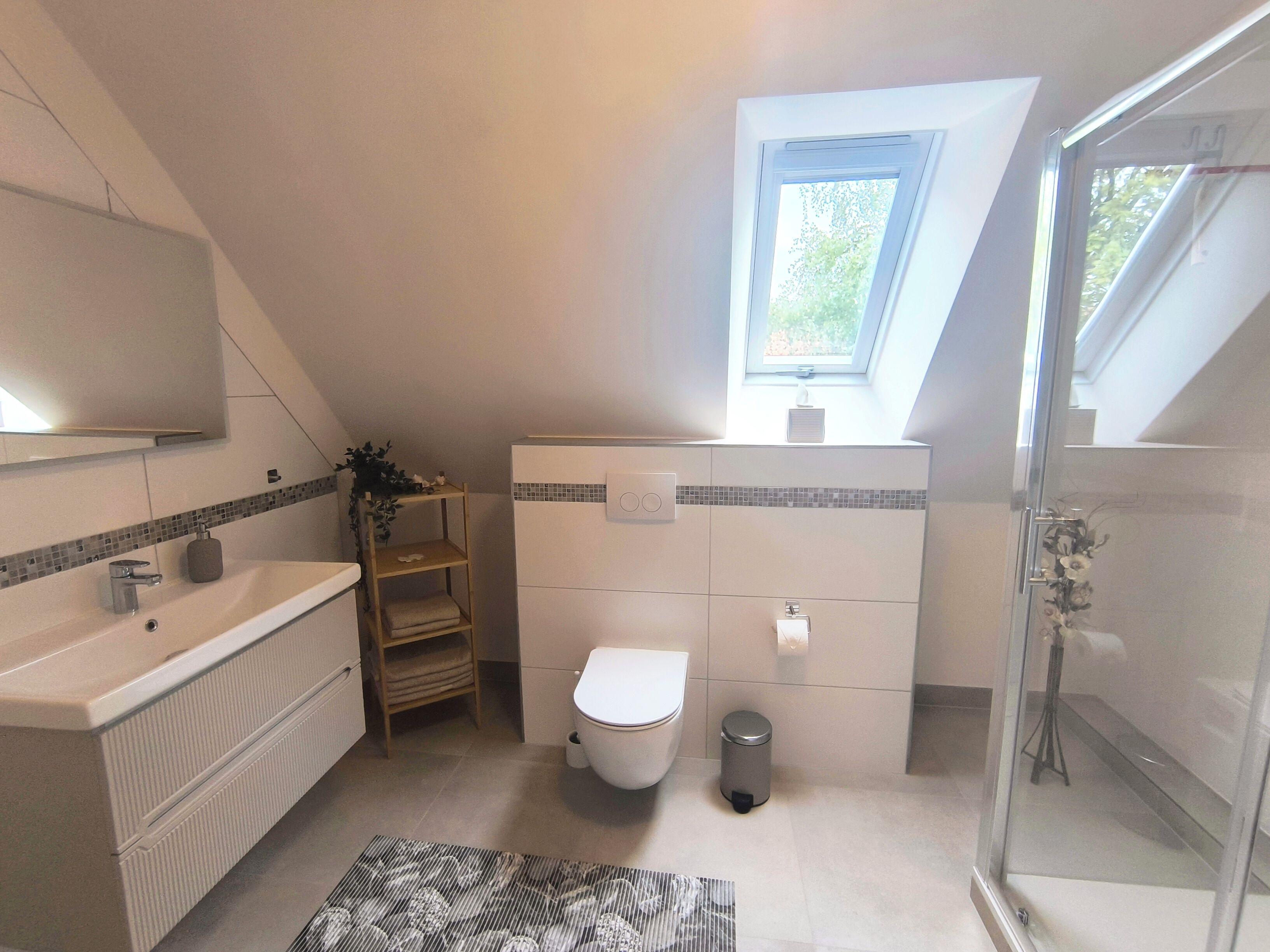 A bathroom with a shower, toilet, sink, and a small window.