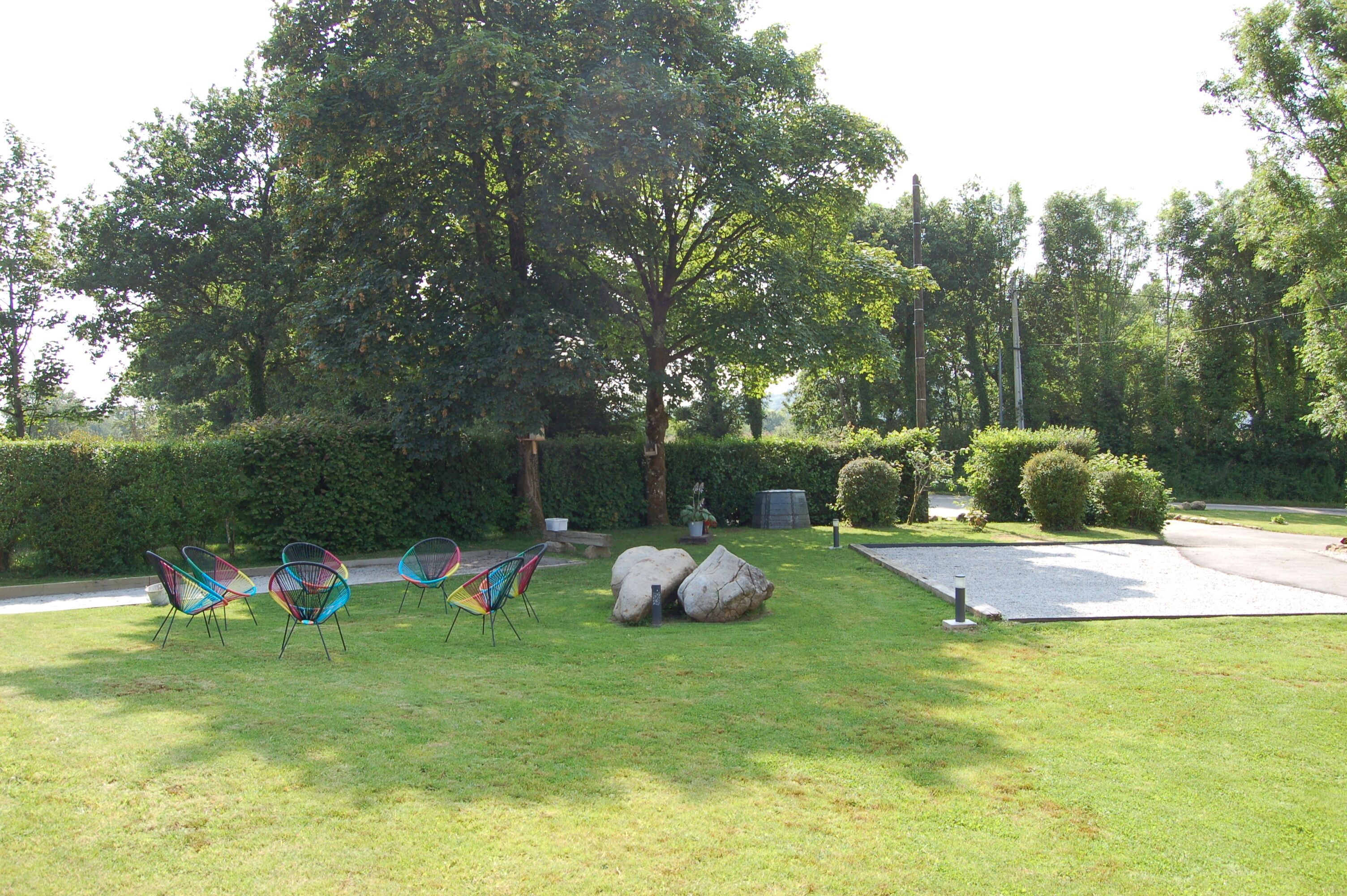 Un espace verdoyant avec des chaises colorées, de gros rochers et des arbres.