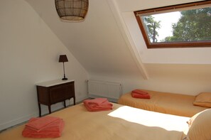 Una habitació amb sostre inclinat, un llit amb roba de llit taronja, una tauleta de nit amb una làmpada i un radiador.