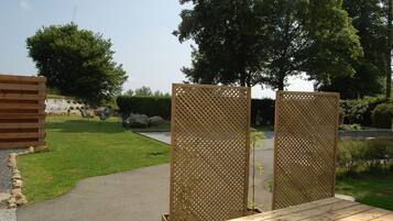 Eine Holzterrasse mit Gitterverkleidung, ein gepflasterter Weg und eine Rasenfläche mit Bäumen und Steinen.