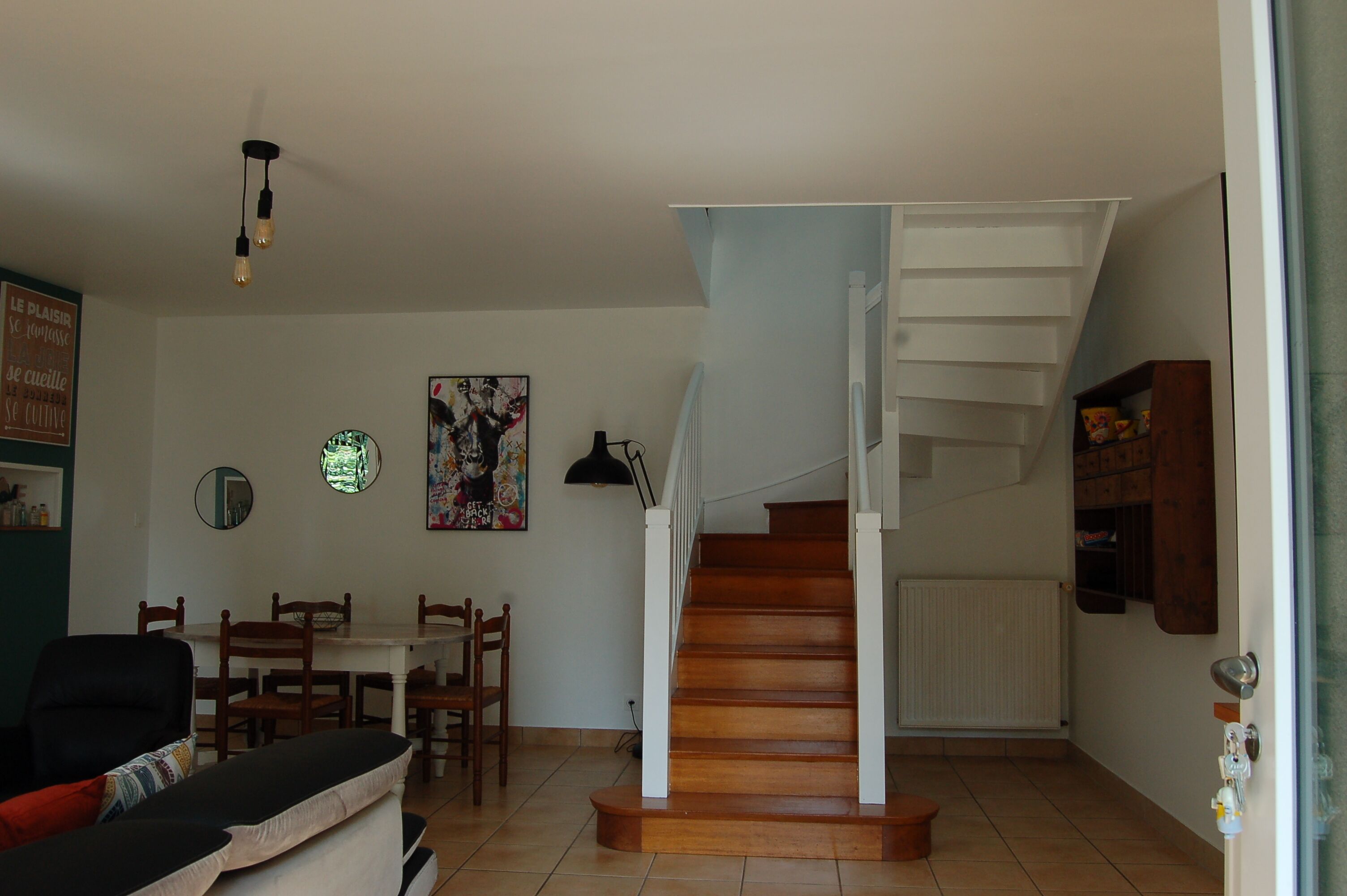 Ein Wohnzimmer mit Esstisch, Stühlen, einer Couch, einer Treppe und einer Heizung.