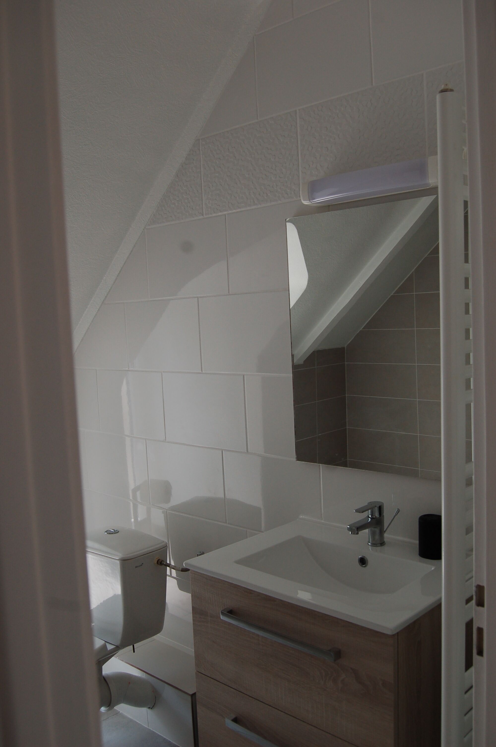 A bathroom with white tiles, a sink, a mirror, and a toilet.