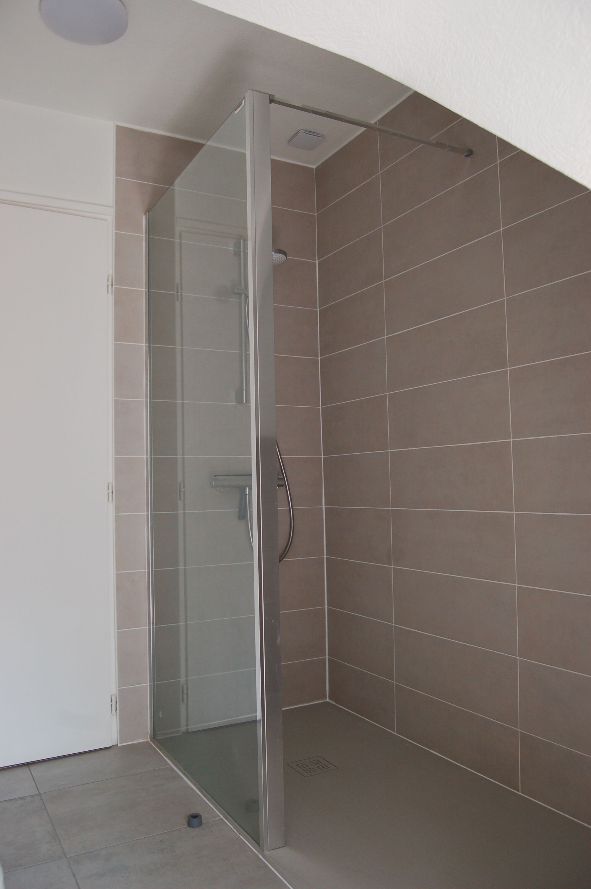 Une salle de bain moderne avec une douche à parois de verre, des murs carrelés et une porte.