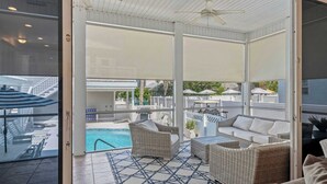 A covered outdoor area with wicker furniture, a pool, and a view of the surrounding area. - Salt & Sol Free Golf Cart Pool Heat Deals (Destin)
