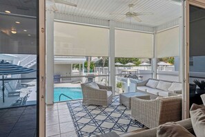 A covered outdoor area with wicker furniture, a pool, and a view of the surrounding area. - Salt & Sol Free Golf Cart Pool Heat Deals (Destin)