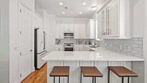 A modern kitchen with white cabinetry, a central island with stools, and a microwave. - Salt & Sol Free Golf Cart Pool Heat Deals (Destin)