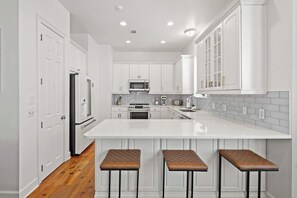 A modern kitchen with white cabinetry, a central island with stools, and a microwave. - Salt & Sol Free Golf Cart Pool Heat Deals (Destin)