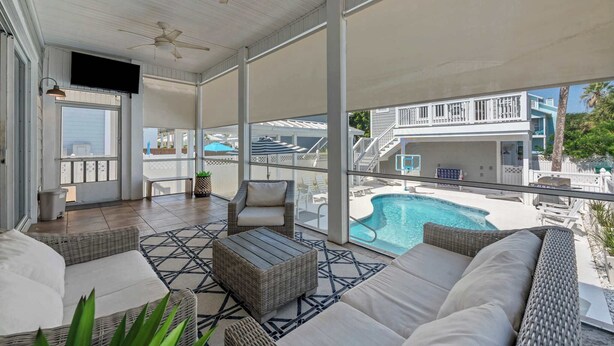 A covered outdoor area with wicker furniture, a pool, and a view of a building with a balcony. - Salt & Sol Free Golf Cart Pool Heat Deals (Destin)