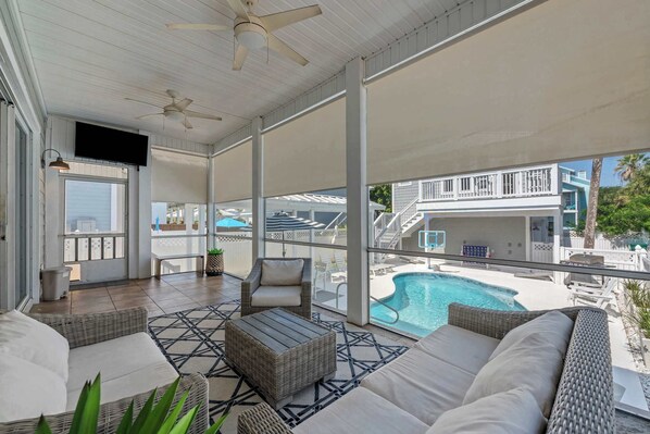 A covered outdoor area with wicker furniture, a pool, and a view of a building with a balcony. - Salt & Sol Free Golf Cart Pool Heat Deals (Destin)
