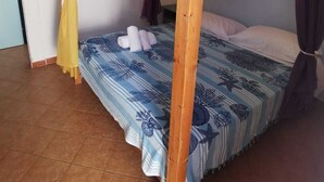 A single bed with a wooden frame, a blue and white patterned bedspread, and two curtains tied at the corners.