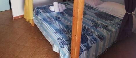 Una cama individual con estructura de madera, una colcha de rayas azules y blancas, y dos cortinas atadas en las esquinas.