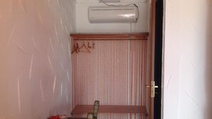A small room with a wooden bench, a red cup, a remote control, and a wall-mounted air conditioner.
