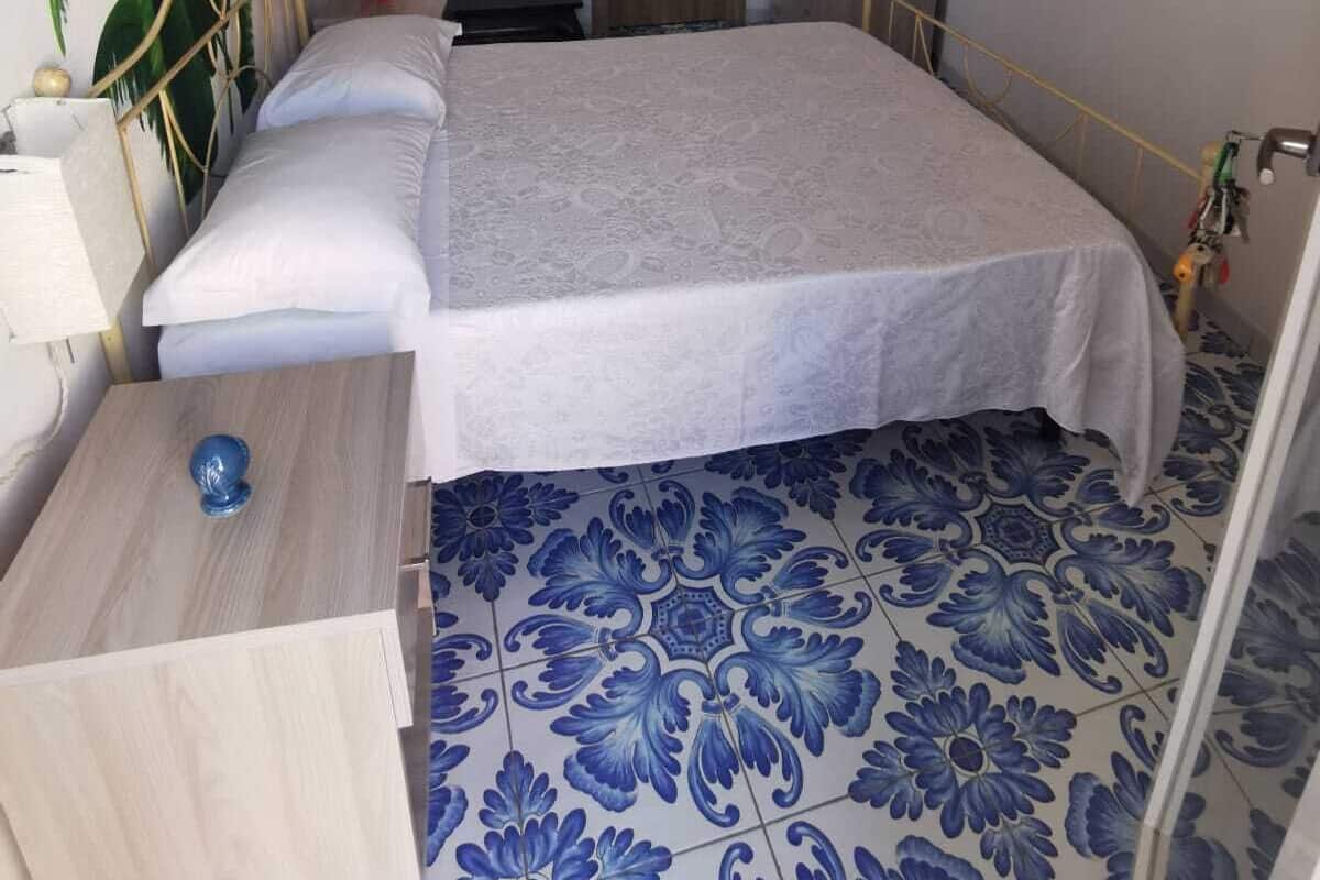 A bedroom with a bed, a nightstand, a wardrobe, a television, and a wall-mounted light fixture.