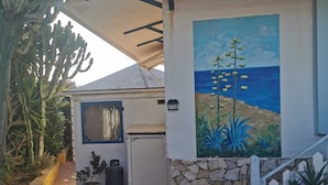 A building with a stone wall, a mural of a coastal scene, and a cactus plant.