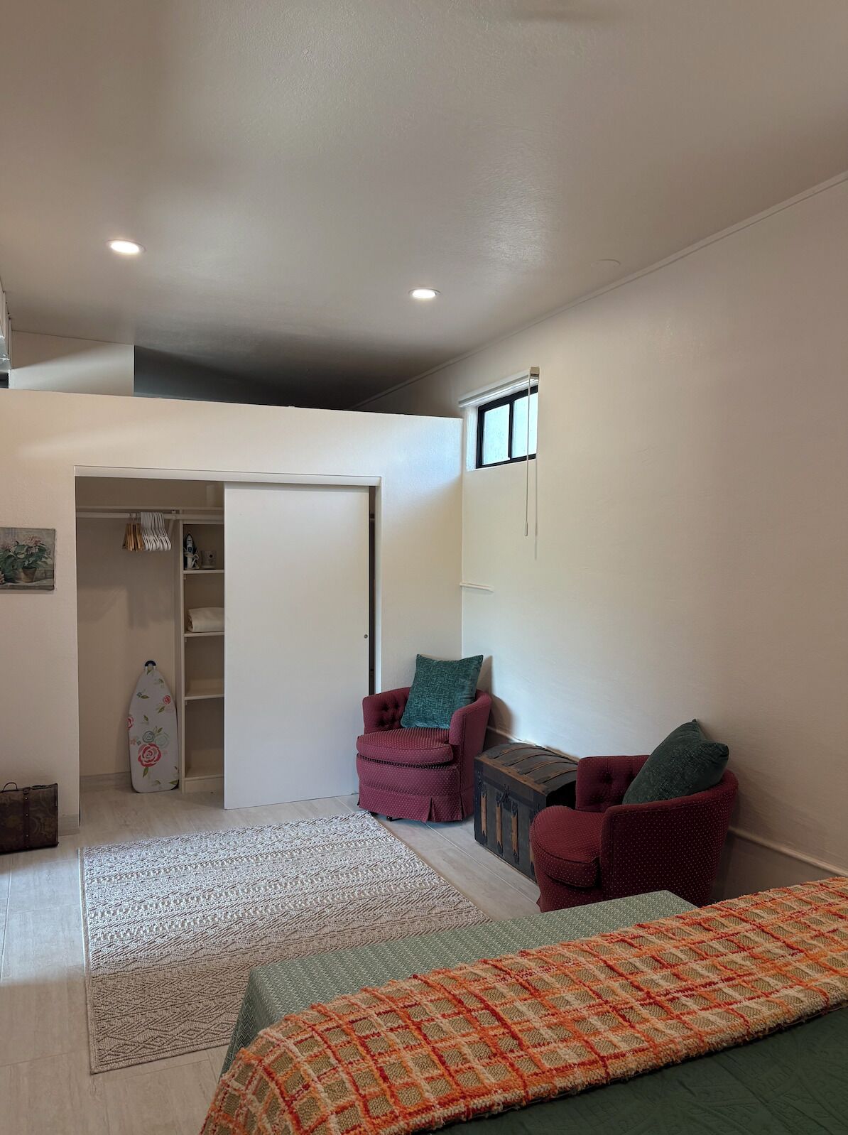 Habitació petita i acollidora amb un llit, dues butaques, una taula petita, una finestra i una porta que dona a un armari.