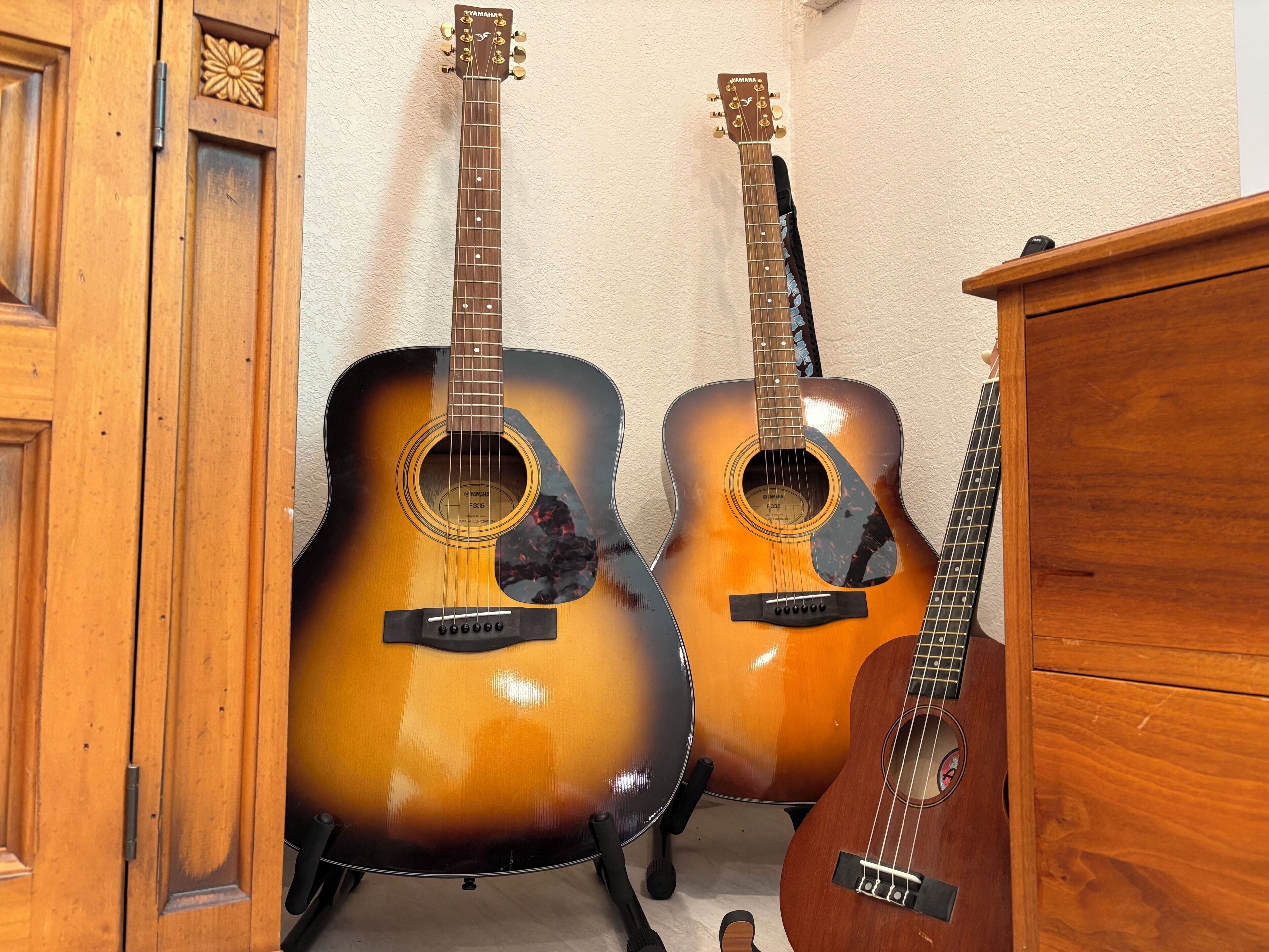 To akustiske guitarer med Yamaha-branding, placeret op ad en væg med et træskab i nærheden.