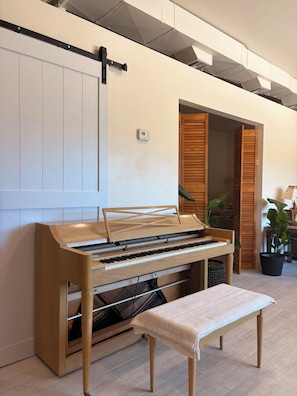 Ein Klavier mit einer Bank, eine weiße Wand, eine Holztür und ein Topfpflanze.