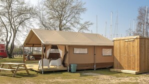 Ein Campingplatz mit Zelt, Picknicktisch, einer kleinen Holzhütte und einem Spielplatz im Hintergrund.