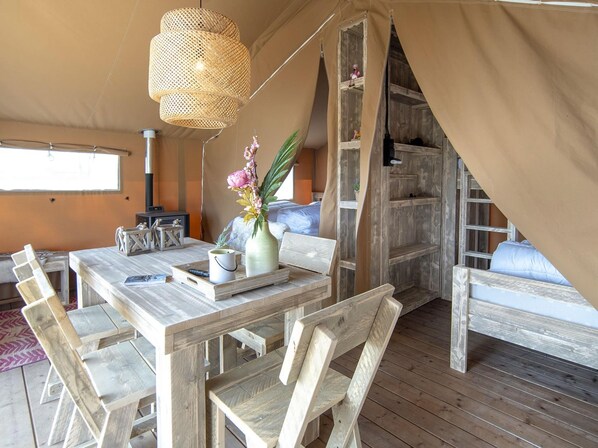 A tented accommodation with a wooden dining table, chairs, a hanging light fixture, and a bed with a view. - Luxury Safari Lodge Escape for 5 (Almere)