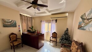 Ein Wohnzimmer mit Deckenventilator, einer Rezeption, zwei Stühlen, einem Sofa, einem Weihnachtsbaum und einem Gemälde an der Wand.