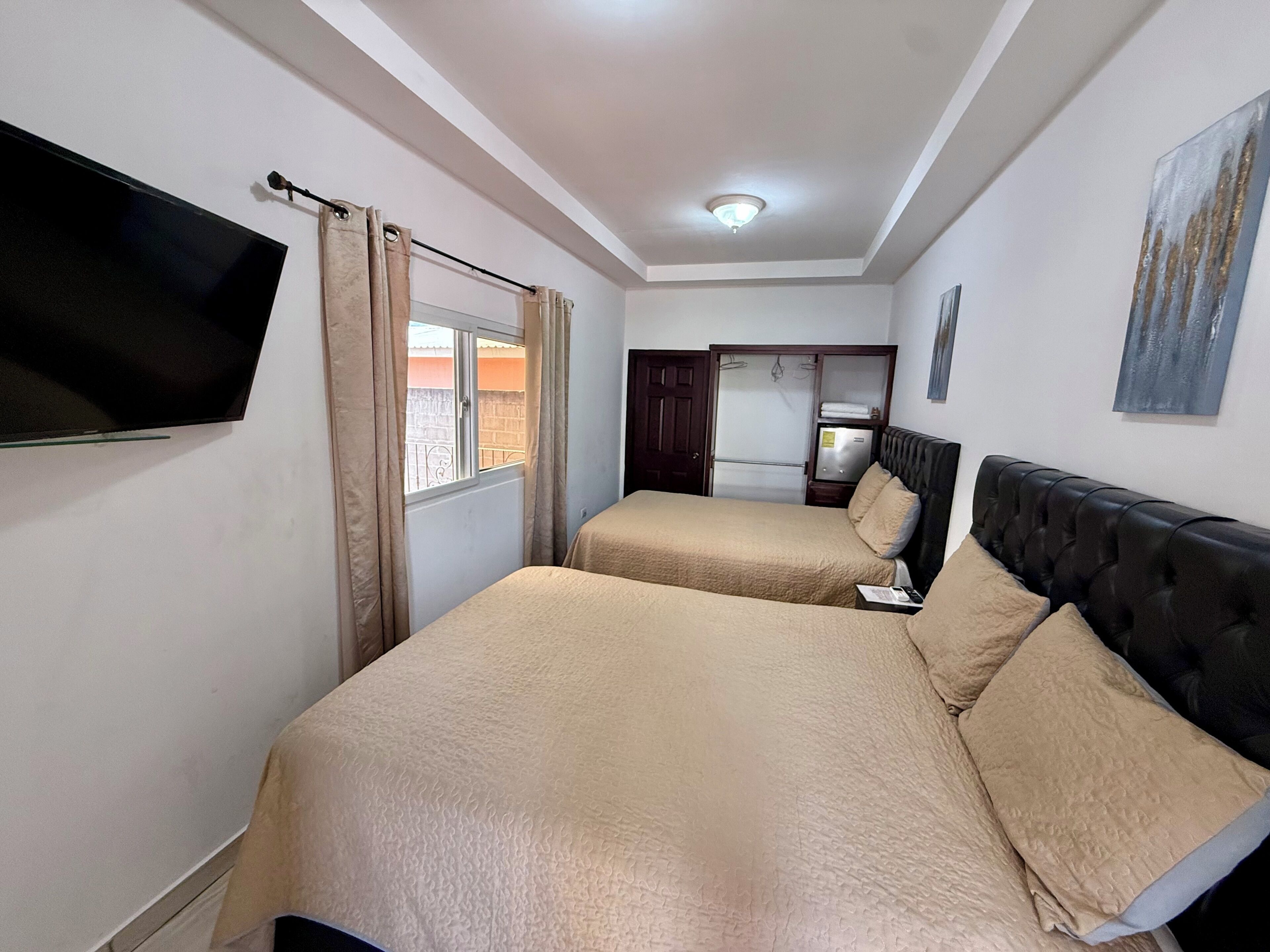 A bedroom with two beds, a TV, a wardrobe, and a painting on the wall.