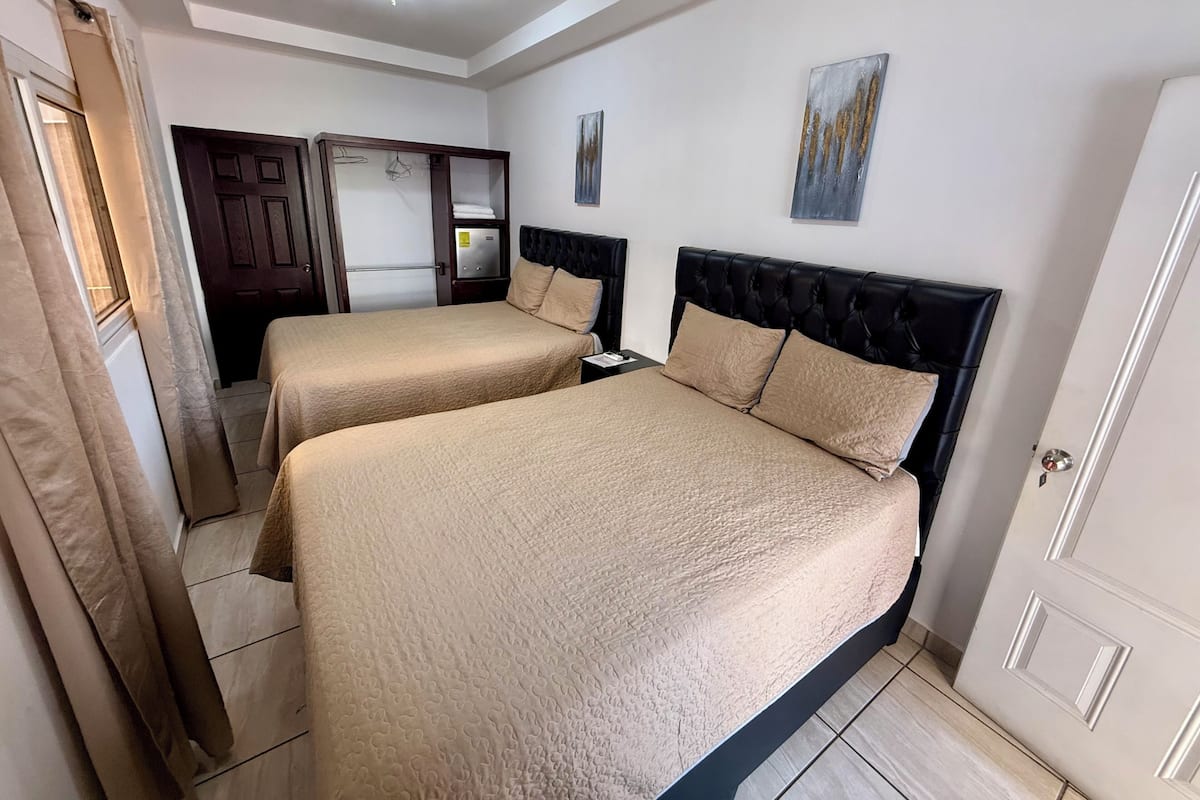 Habitación de hotel con dos camas, un armario, una puerta y una lámpara en el techo.