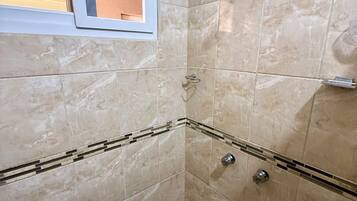 Eine Dusche mit Handbrause, einem Fenster und einem gefliesten Boden.