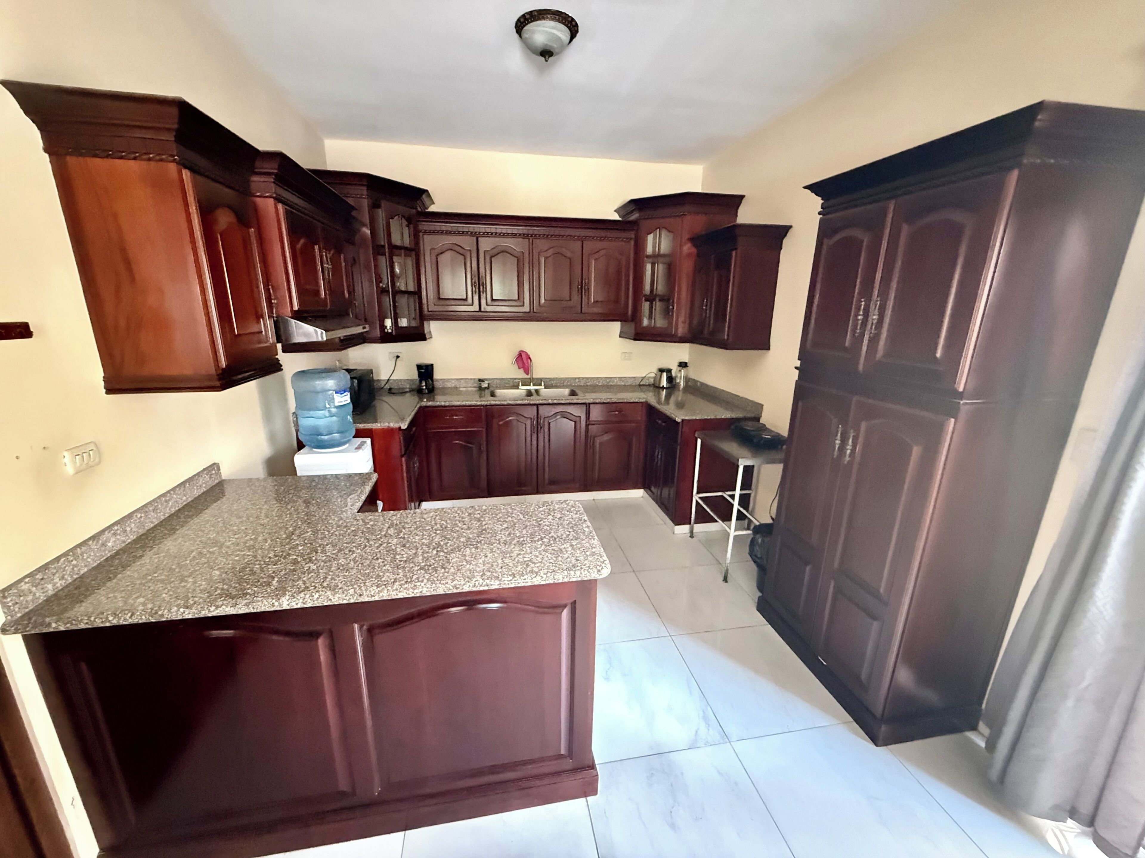 A kitchen with dark wooden cabinets, a granite countertop, and a water dispenser.