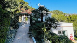 A pathway leading to a modern building with a satellite dish, surrounded by lush greenery and trees. - Contemporary hillside villa with sea view (3 kms) (Xàbia)