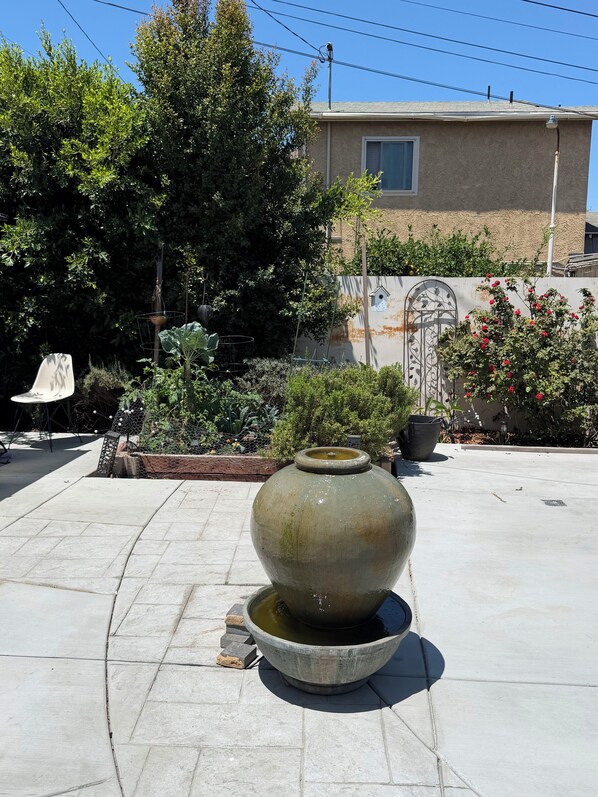 A courtyard with a large stone fountain, a white chair, and a variety of plants.