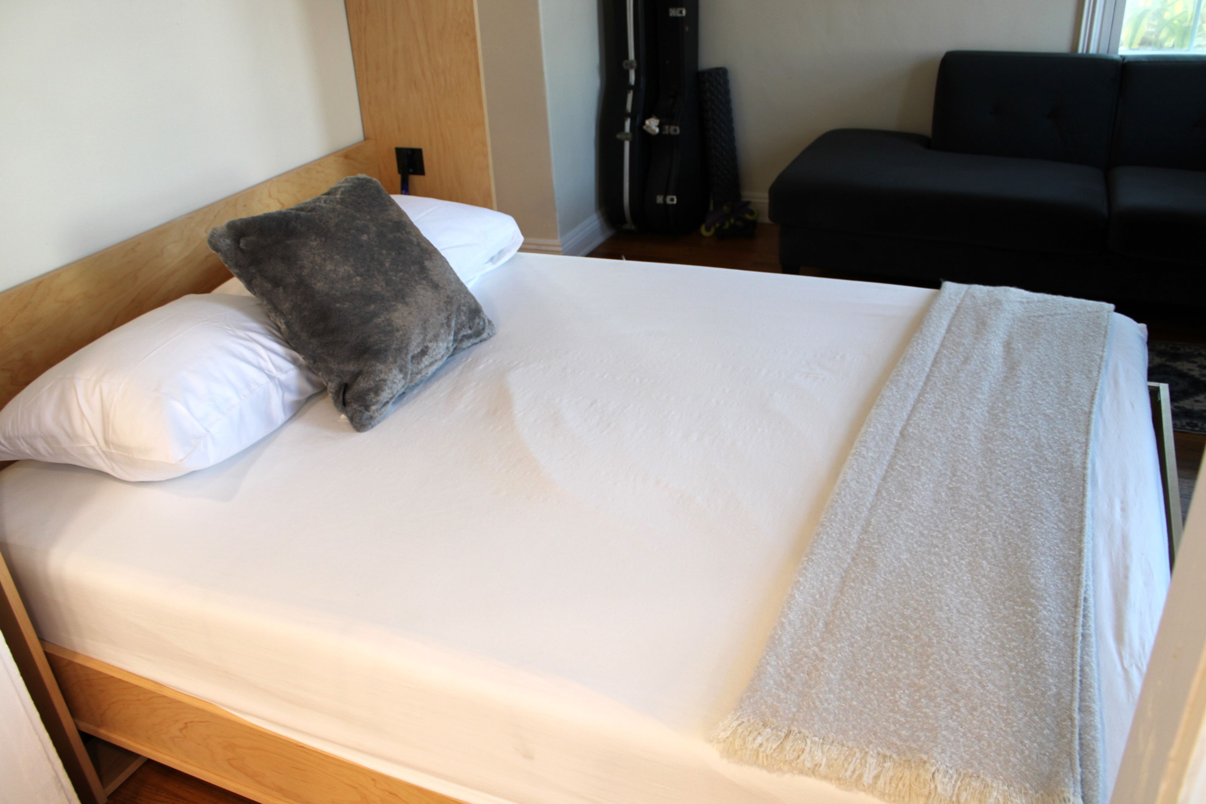 A neatly made bed with a white mattress, a grey pillow, and a white blanket.