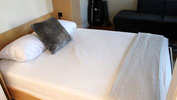 A neatly made bed with a white mattress, a grey pillow, and a white blanket.