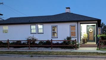 A single-story house with a dark roof, white walls, and a front door with a decorative design.