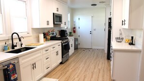 Una cucina moderna con mobili bianchi, lavastoviglie in acciaio inox, microonde e piano cottura.