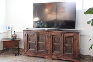 Un meuble en bois surmonté d’un téléviseur à écran plat, une petite table ornée de bouteilles décoratives et une plante sur la droite.