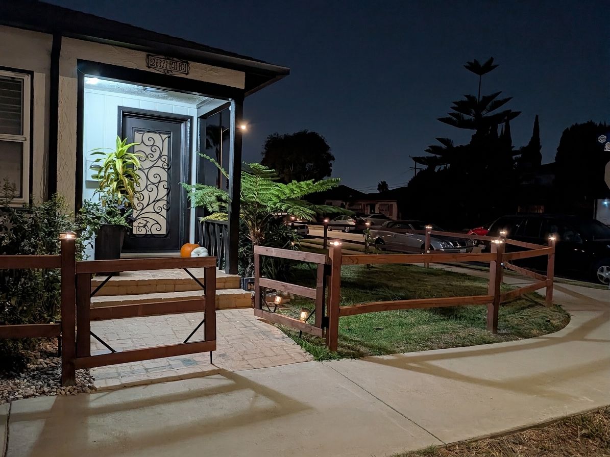 A gated entrance to a building with a well-lit door and a small garden area with plants.