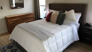 A bedroom with a bed, a wooden dresser, a nightstand, a lamp, and a mirror on the wall.
