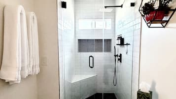Une salle de bain moderne avec une douche à parois de verre, des murs recouverts de carreaux blancs, des toilettes et un porte-serviettes.