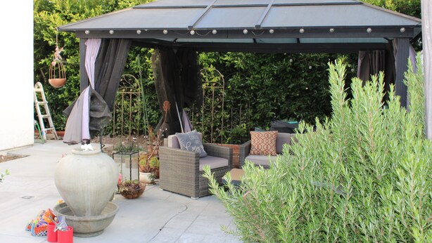 Un’area patio coperta con mobili da esterno, un vaso grande e una struttura a pergola.