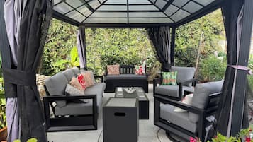 A covered outdoor seating area with a glass roof, black furniture, and potted plants.