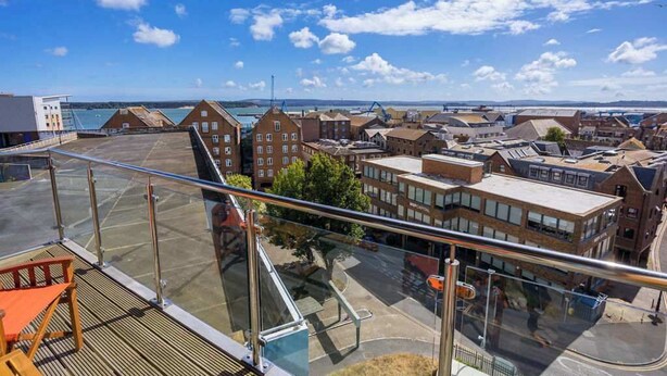 En høj bygning med en glasbalkon med udsigt over en kystby.