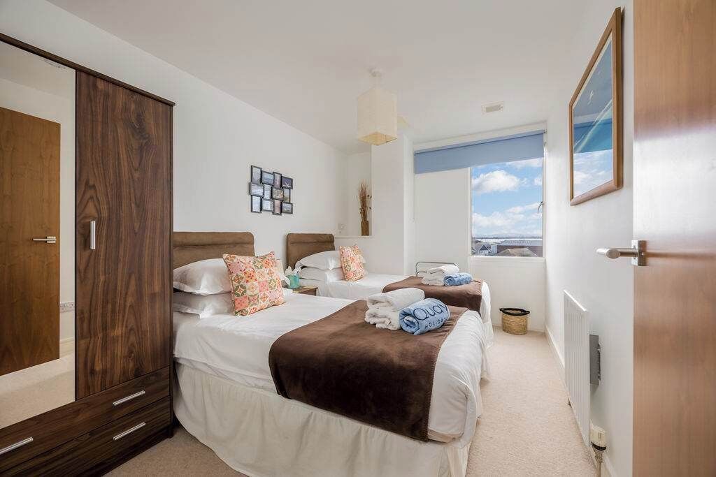 A hotel room with two beds, a wardrobe, a view of the city, and a window.