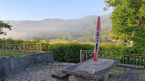 Una panchina di pietra con un tavolo, una bandiera e una vista su un paesaggio montano avvolto nella nebbia.