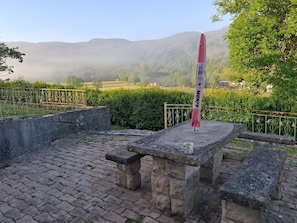 Eine Steinsitzbank mit Tisch, einer Flagge und Blick auf eine nebelverhangene Berglandschaft.