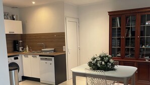 Cucina moderna con mobili bianchi, lavastoviglie e macchina da caffè. Zona pranzo con tavolo e sedie, e pensile con ante in vetro.