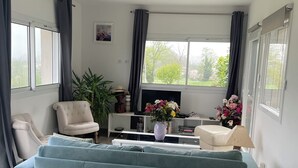 Un soggiorno moderno con un ampio divano blu, una TV a schermo piatto, un tavolino da caffè con un vaso di fiori e una libreria.